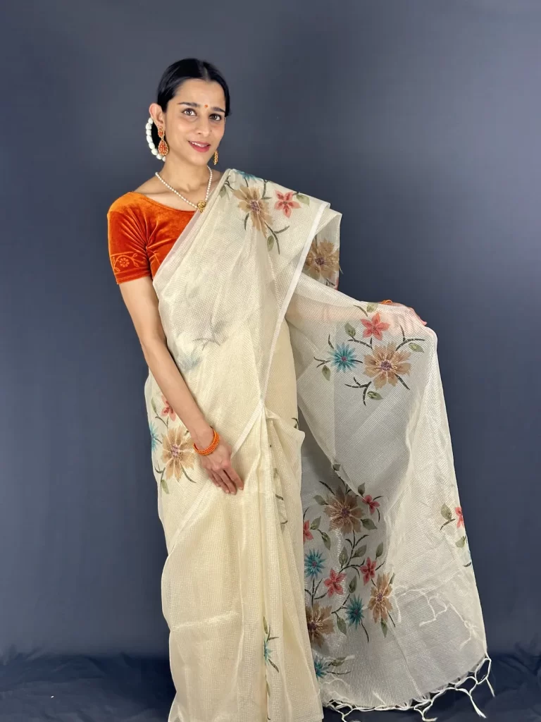 Model holding the floral pallu of Golden Floral Tissue Kota Saree with an orange blouse