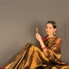 Golden Radiance saree in a seated pose holding a mirror