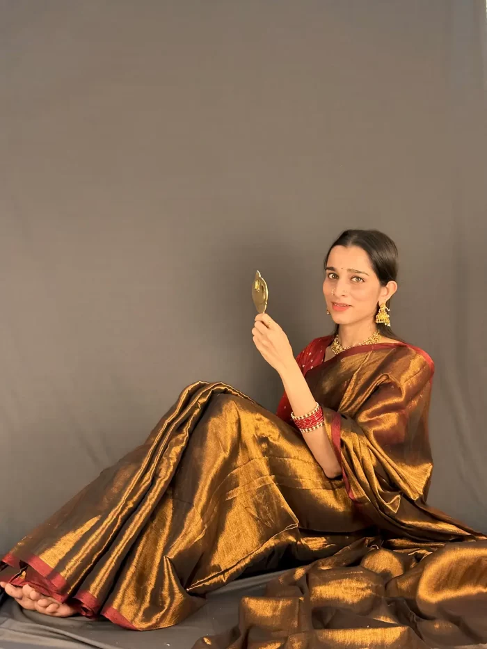 Golden Radiance saree in a seated pose holding a mirror