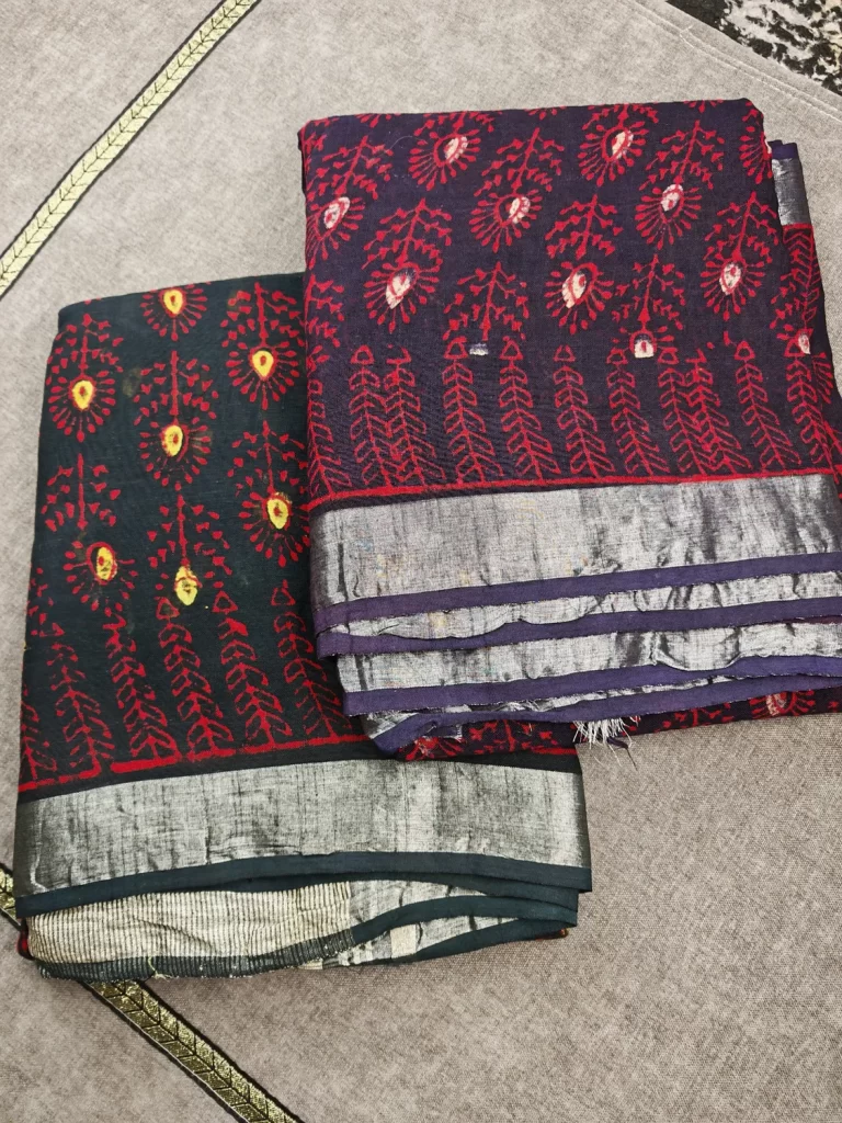 Two folded Crimson Bloom sarees with red floral motifs and silver-toned borders