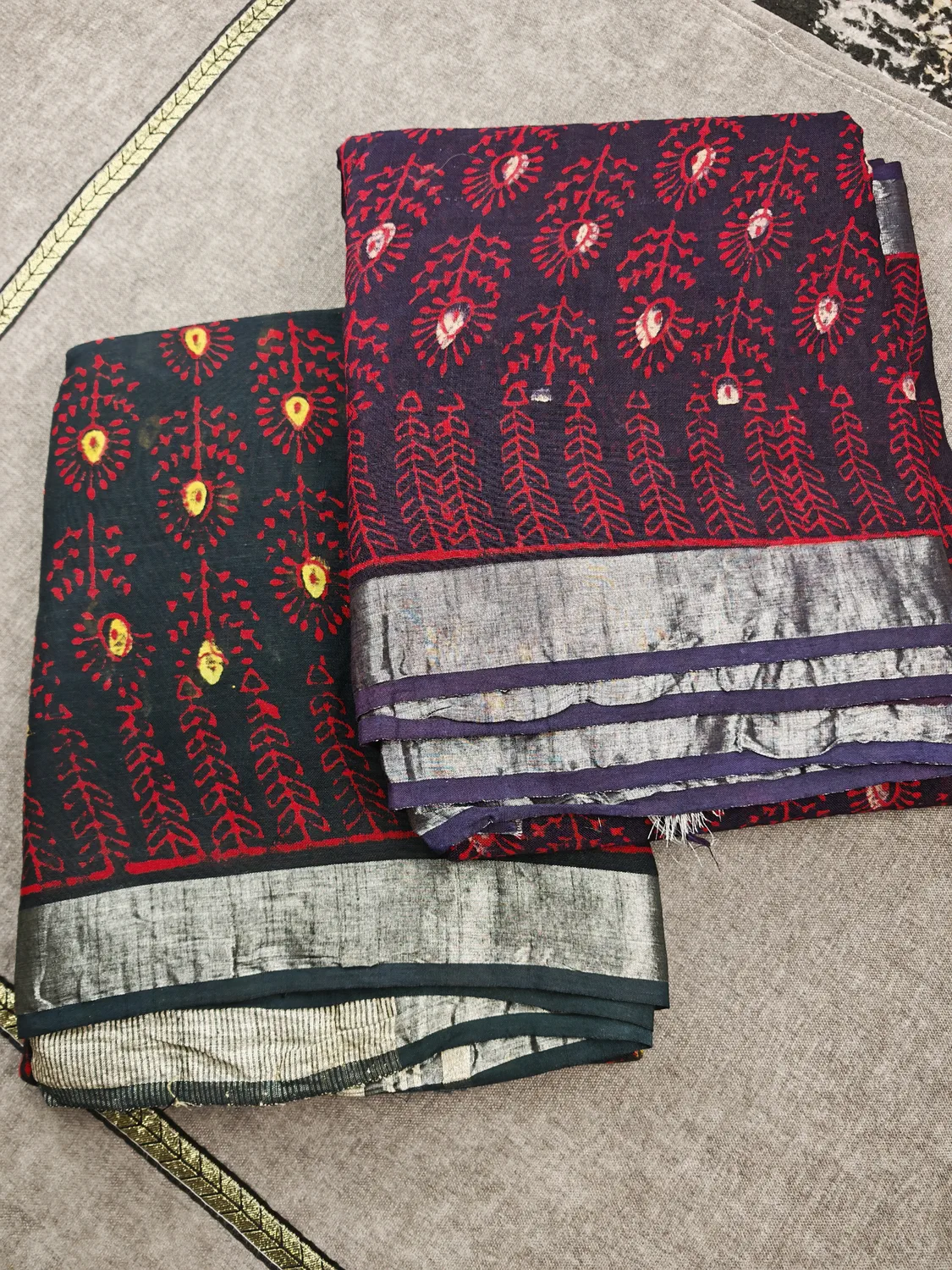 Two folded Crimson Bloom sarees with red floral motifs and silver-toned borders
