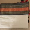 Offwhite Mulcotton Saree with Black & Orange Border (11) Folded Off-White Mul Cotton Saree showing the black-orange woven border and red-black tassels