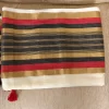 Folded off-white saree showing red, black and golden striped border with tassel