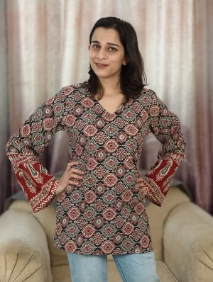 Model wearing a rust Ajrakh short kurti with a V-neck and wide bell sleeves, paired with blue jeans