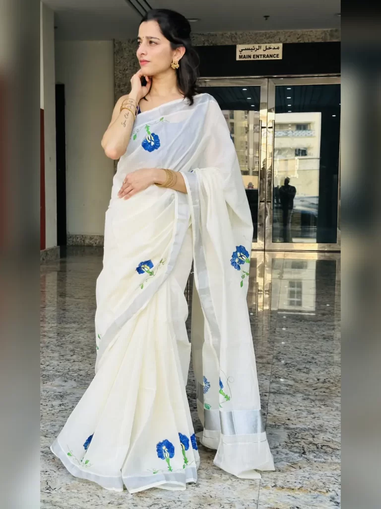 Shangupushpam hand-painted ivory saree with blue floral motifs and silver border – full-length front view