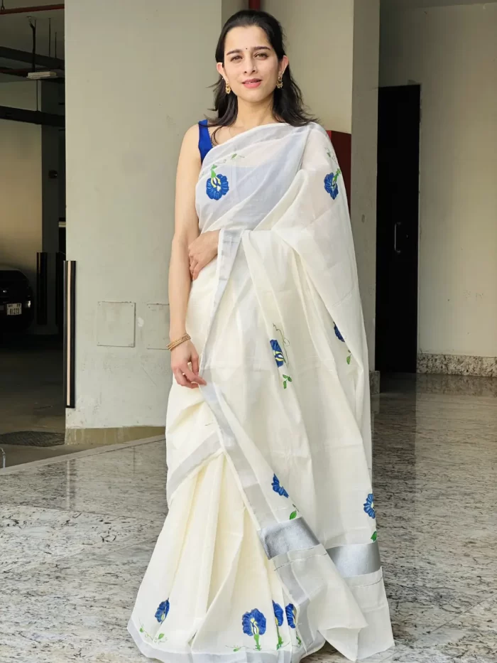 Shangupushpam Hand-Painted Saree – Front View Front view of Shangupushpam ivory saree with blue floral painting and silver border