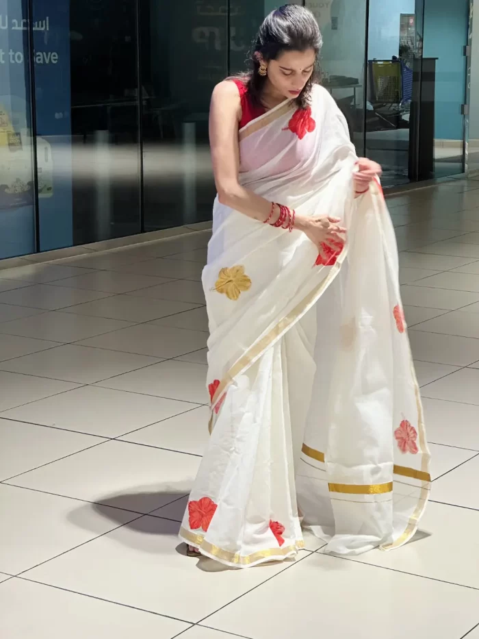 Chembarathi Hand-Painted Saree – Draped View Chembarathi white hand-painted saree with red hibiscus motifs and gold border – draped front view